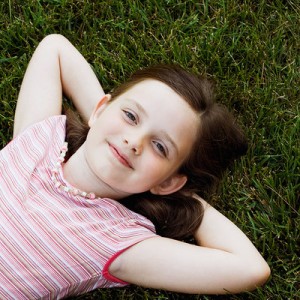 A pretty young girl, lying in the grass with her arms behind her head.
