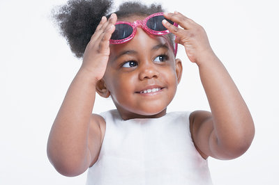 A young African American girl lifts off a pair of sparkly red sunglasses.