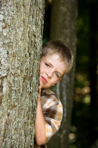 A young boy peeks around the side of a tree.