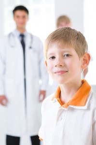 A young boy stands in the foreground. Behind him we can see his doctor.