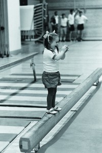 A young girl with Down syndrome stands on the balance beam in gym class.