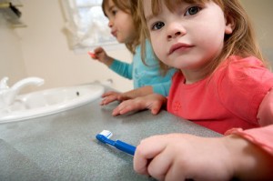 Close-up of a young girl, toothbrush in hand, but looking us straight in the eye.