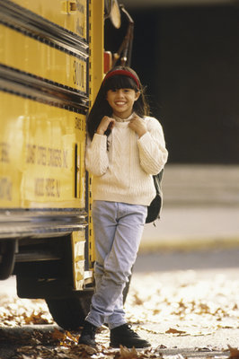 Pretty elementary school age girl is standing next to her school bus.