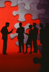 Conceptual picture of a group of people, backlit by the parts of a puzzle that need to go together.