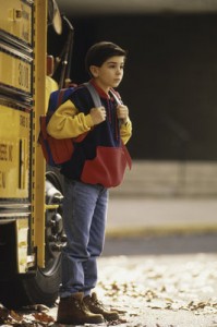 An elementary school-age boy, with backpack, gets off the school bus.