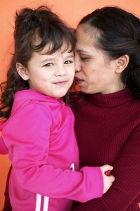 Picture of a mother holding her toddler, nuzzling near her ear. Foto de una madre abrazando a su hija.