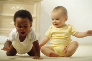 Two babies side by side, one crawling, one sitting and watching.