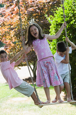 Foto de una chica, jugando con sus hermanos menores. A young girl plays loudly with her brothers and sisters on a swing.