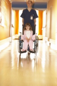 En el pasillo de un hospital, una enfermera empuja la sillón de ruedas de una muchacha joven.