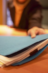 Closeup of someone passing a blue folder bulging with information across the table.