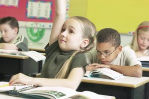 Girl student in the middle of the class enthusiastically raises her hand to answer.