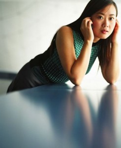 A teenage Asian girl leans on her elbows on a glossy-topped table, waiting.