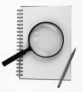 Photo of a notebook, with a magnifying glass and a pen on top.