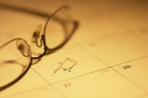 Photo of a desk calendar with a pair of glasses atop and a meeting time written in.