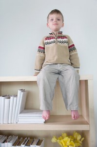 Picture of a young boy, sitting atop a bookshelf in the classroom.