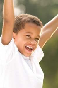 Photo of a young African-American boy, lifting his arms up high and grinning.