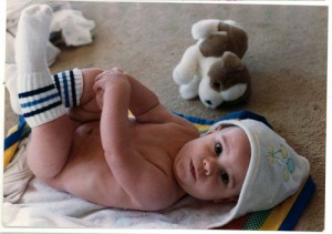 Photo of a boy baby straight from his bath, lying on his back in a bathtowel, wearing tube socks.