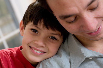 A young boy leans his head against his father's shoulder.