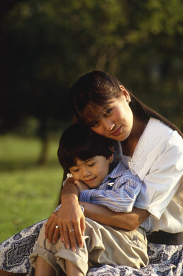 Asian mom holds her son on her lap, with her arms around him.