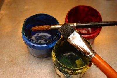 Three pots of colored paint, with brushes atop.