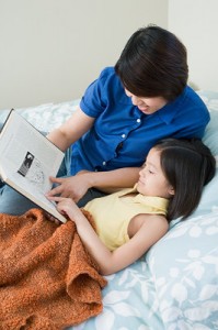 A mom and a young girl lie in bed, sharing a book.