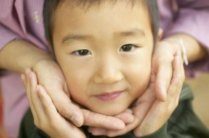 A young Asian boy's face is held tenderly in someone's cupped hands.