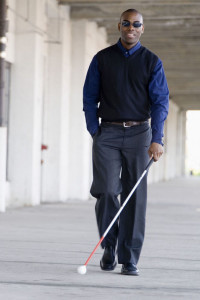 Blind young man walking on the sidewalk, with a white cane