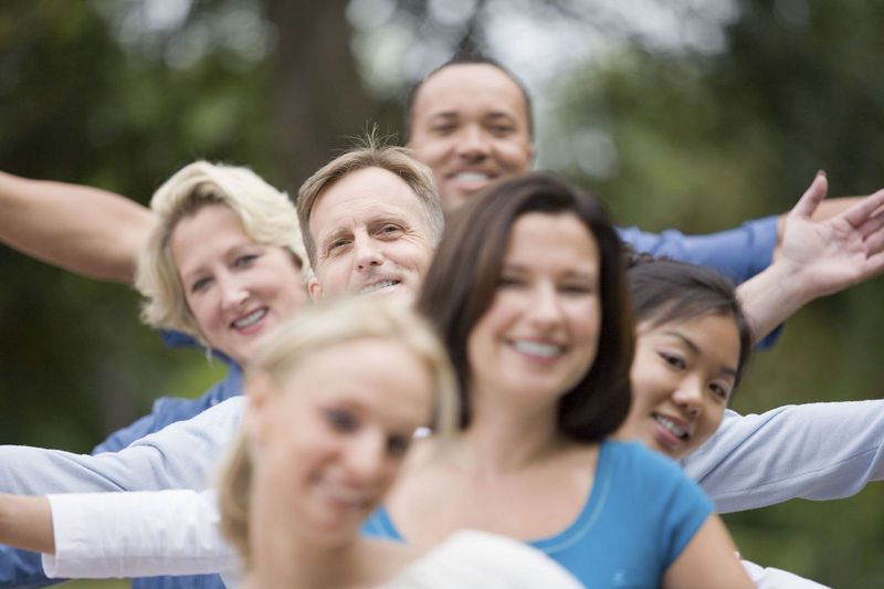 Six smiling people in a line, their arms thrown wide in greeting.