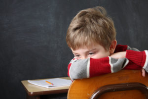 Boy covering face sitting backwards in his classroom chair