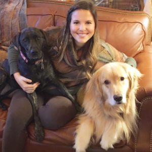 young, smiling woman sitting on couch with her two dogs