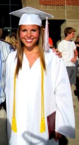 smiling young woman in white high school graduation cap and gown