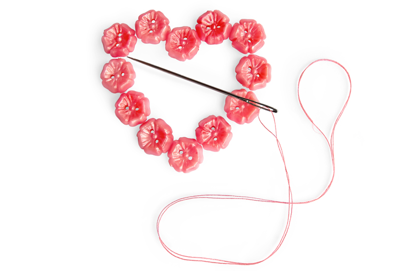 The individual beads of a necklace are being sewn back together again in the shape of a heart.