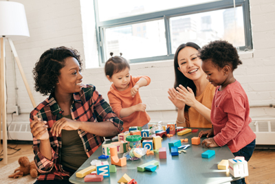 2 parents sit on the floor and play blocks with their young children.