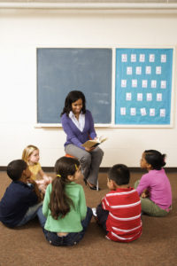 Una maestra leyendo a un grupo pequeno de estudiantes sentados