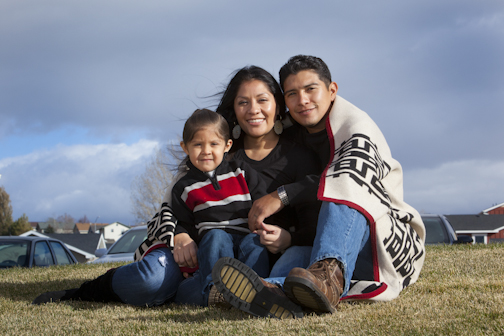 Young Native American family of three pose with a blanket wrapped around them