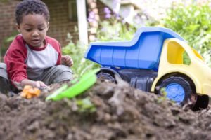 A young African-American boy plays in a dirt pile with his dump truck.