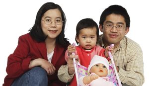 Asian family of mom, dad, and their toddler, who's pushing a stroller with a baby doll in it