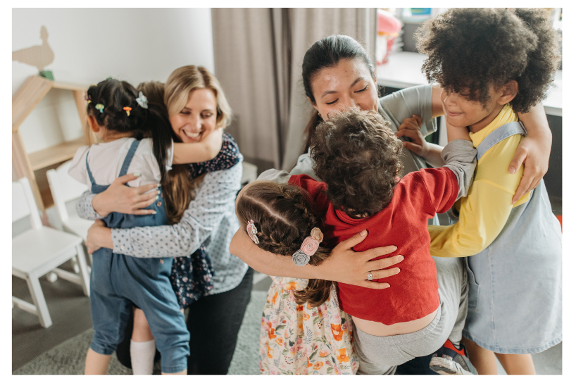 TeachersHuggingChildren Early Childhood teachers hugging children.