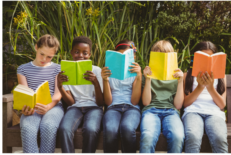 Five children sitting outside on a bench reading books.