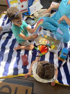 Two young deafblind children playing with toys in a small sandbox with therapist in the background.