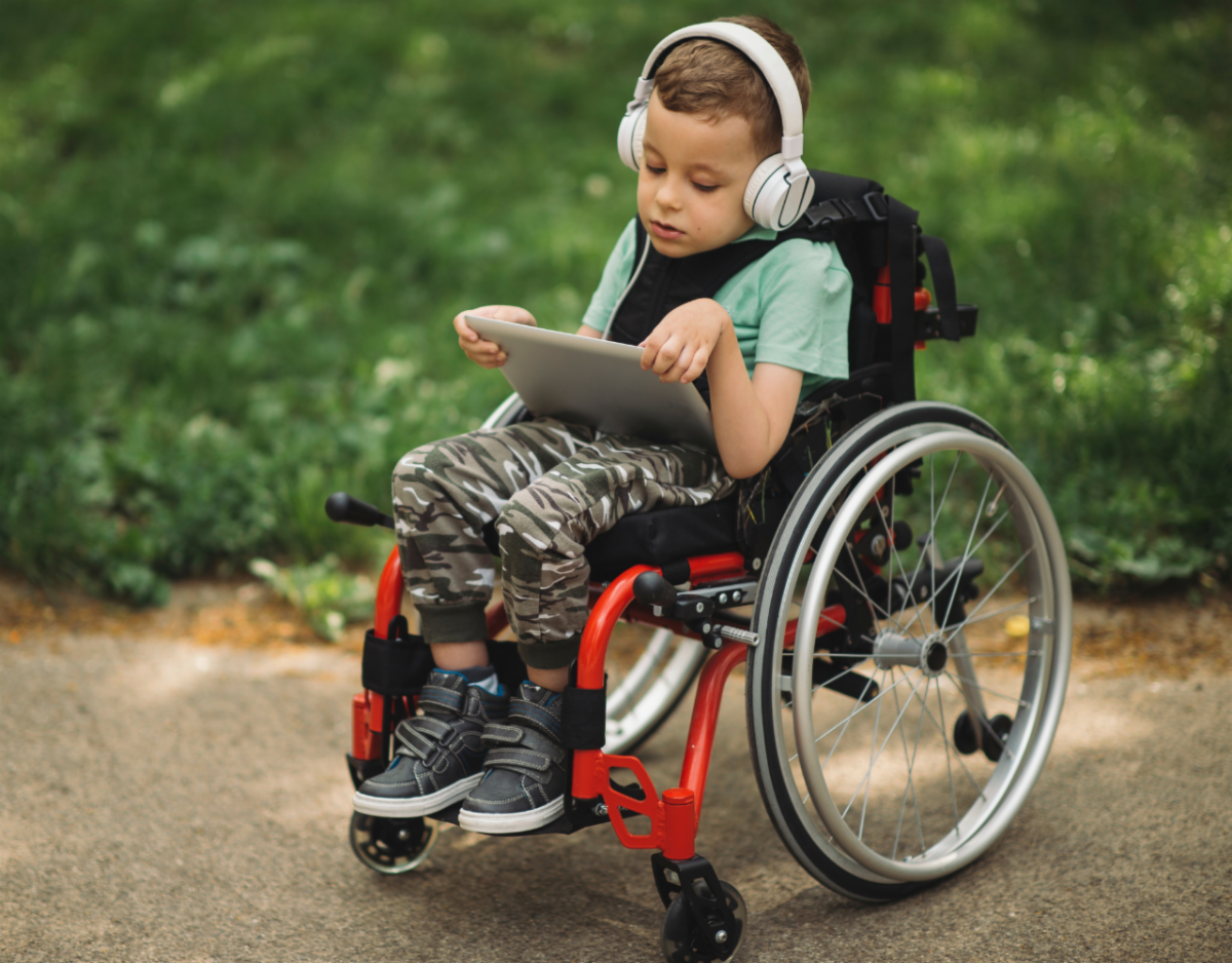 Little boy in a wheelchair holding and watching a tablet.