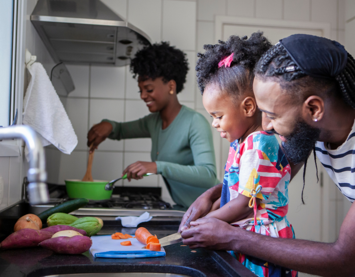 A mom and dad cooking together with their daughter.