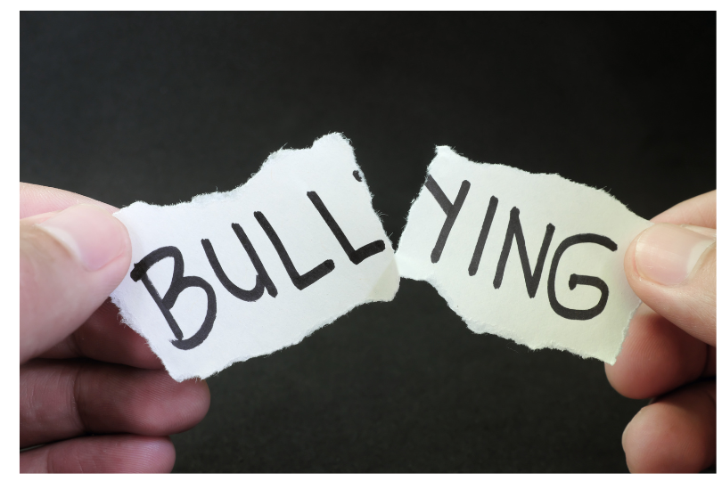 Image showing part of two hands tearing a slip of paper with the word BULLYING on it. 