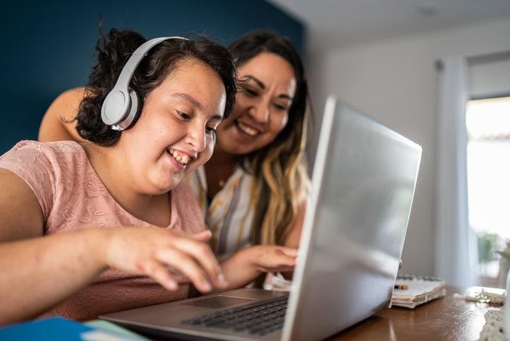 Image of a teenage girl with headphones typing on a computer with mom helping her.
