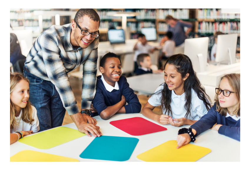 Image of male teacher teaching students sitting at a table. 